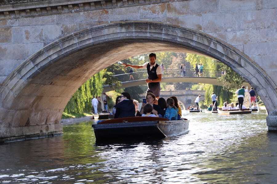 Busy summer punting in Cambridge, with punts on the River Cam seen through a stone bridge arch