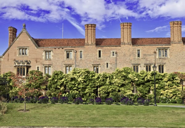Brick and stone buildings of Magdalene College, Cambridge, behind a neat lawn and hedges