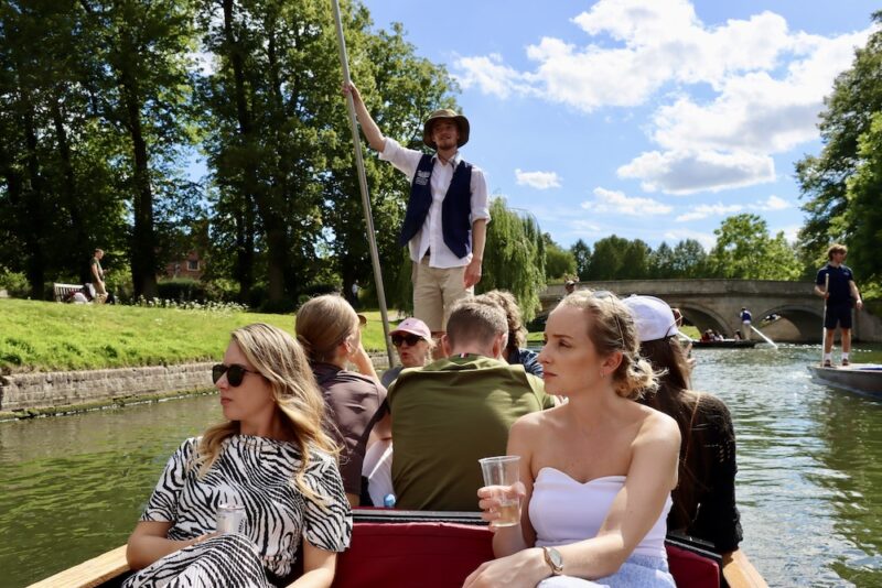 Sunny day River Cam punting tour two women with drinks looking at St Johns College Cambridge