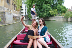 two girls taking a selfie with their box of sushi on a picnic punt, outside St Johns College