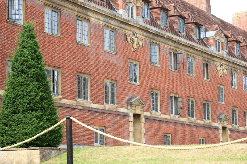 Red-brick college building with a clipped yew tree beside the lawns of the Backs.