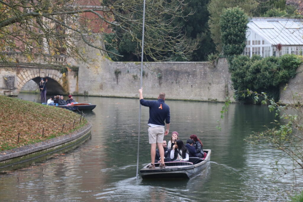 Punt chauffeur guiding guests along the River Cam beside St John's College walls.