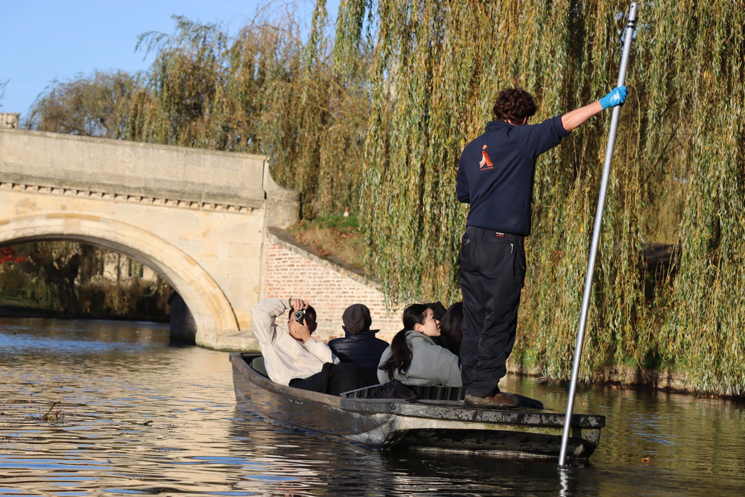 customers on a punting tour in Cambridge with Let's Go Punting with the chauffeur with his back to the camera approaching a bridge