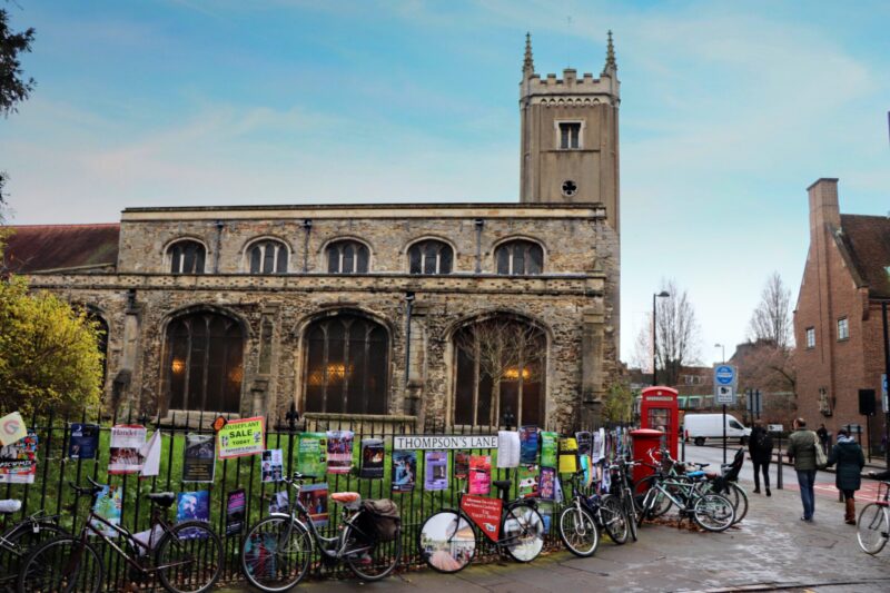 A church on the corner of Thompson's Lane with bikes on the railings and a red telephone box.