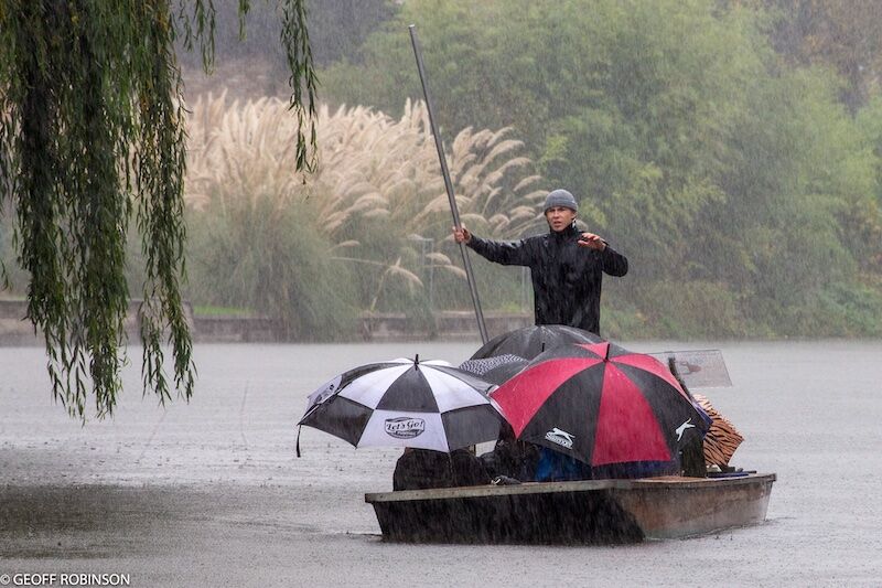 Passengers huddled beneath umbrellas on a chauffeured punt during heavy rain in Cambridge.