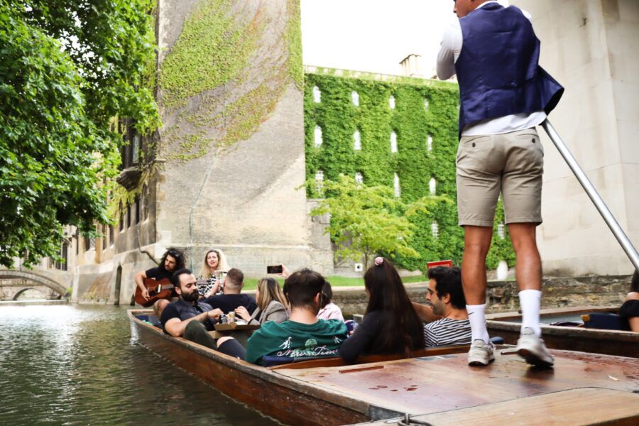 Guests on a chauffeured punt listening to live music beside the ivy-clad walls of St John's College.