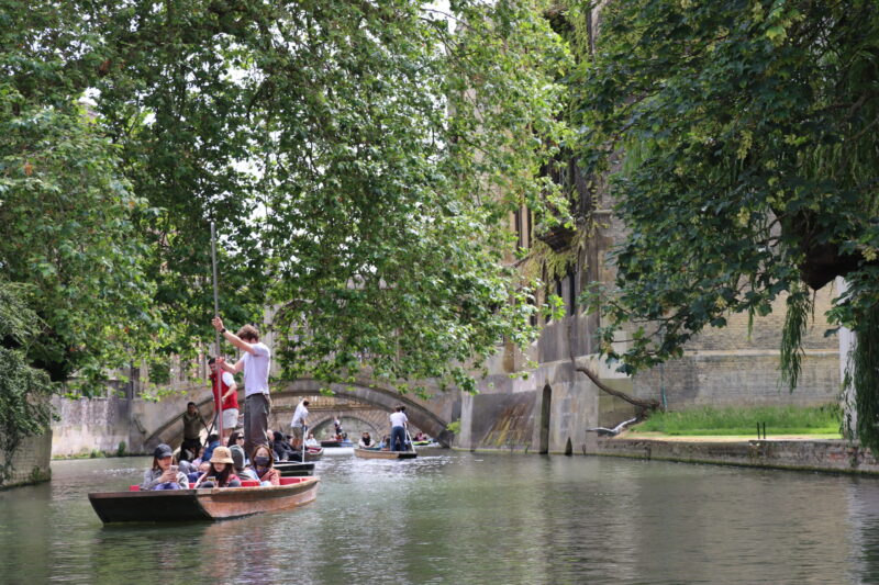Punting boats going through St John's College Cambridge on The Backs under leafy trees.