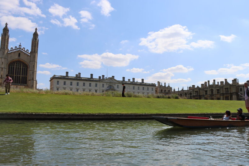 Kings College Chapel and lawns seen from the River Cam with a punt passing on a sunny day.