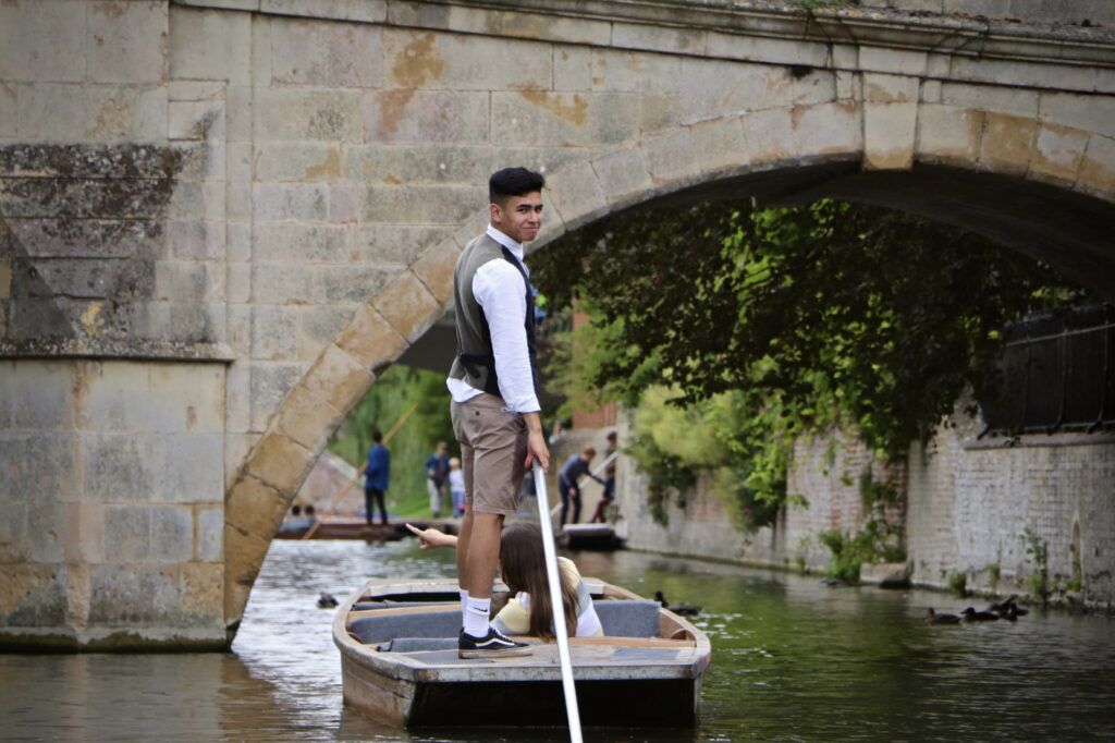 Let's Go Punting chauffeur in a waistcoat steering a punt under a stone bridge.