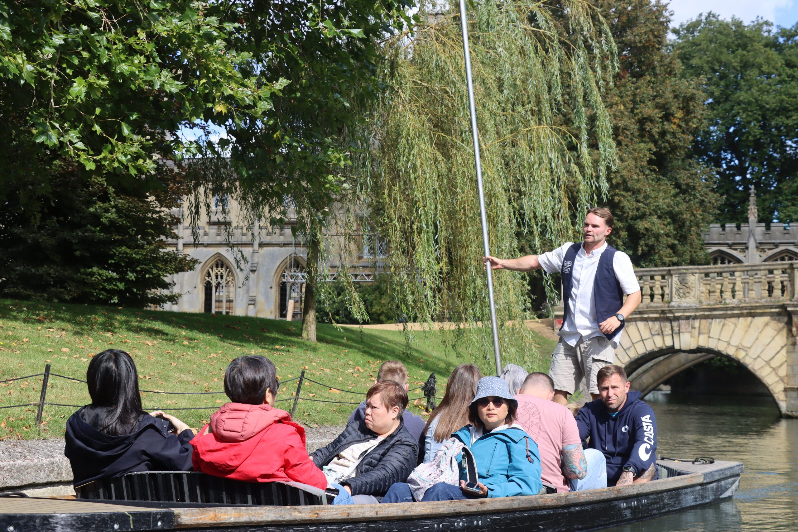 Customers on a punting tour in Cambridge with a bridge in the background and chauffeur holding the pole
