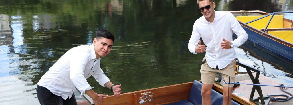 Two members of the Let's Go Punting team in white shirts posing on punts at the station.
