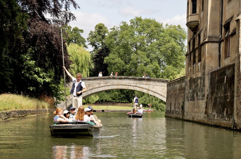 Two punts on the River Cam near Clare Bridge, framed by trees and college stonework.