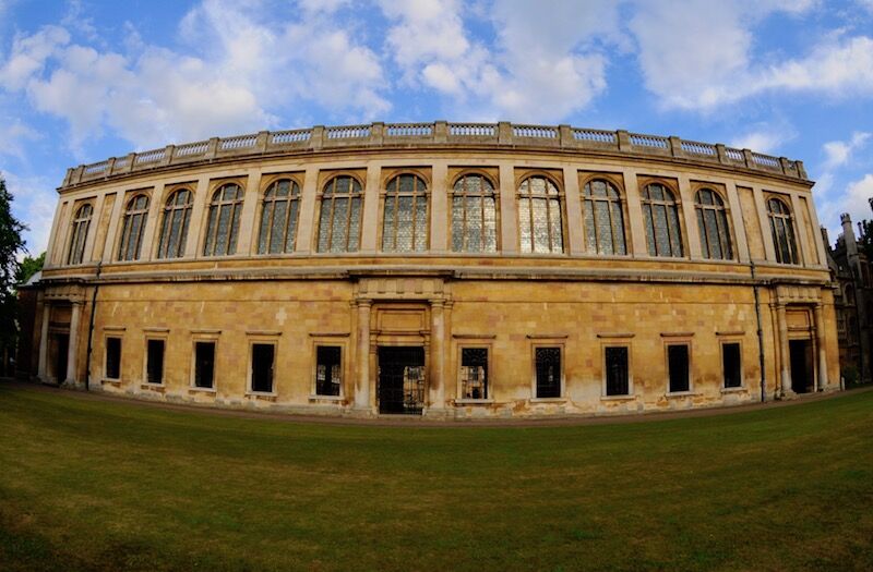 Wide view of the Wren Library at Trinity College Cambridge behind a neat lawn.