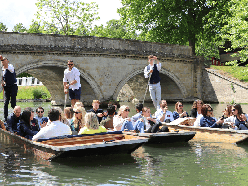 Three punts carrying a large group on a punt tour beside a stone bridge on the River Cam.