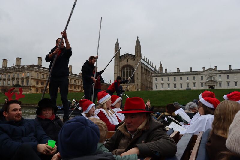 Guests on punts in Santa hats enjoying Carols on the River beside King's College Chapel.