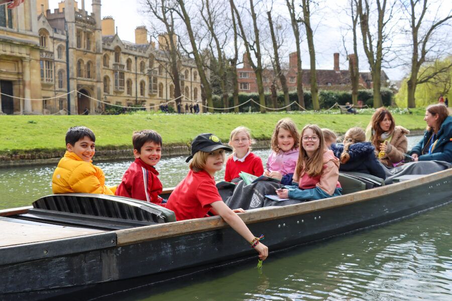 Group of schoolchildren on a punt on the River Cam passing college lawns on a school trip.