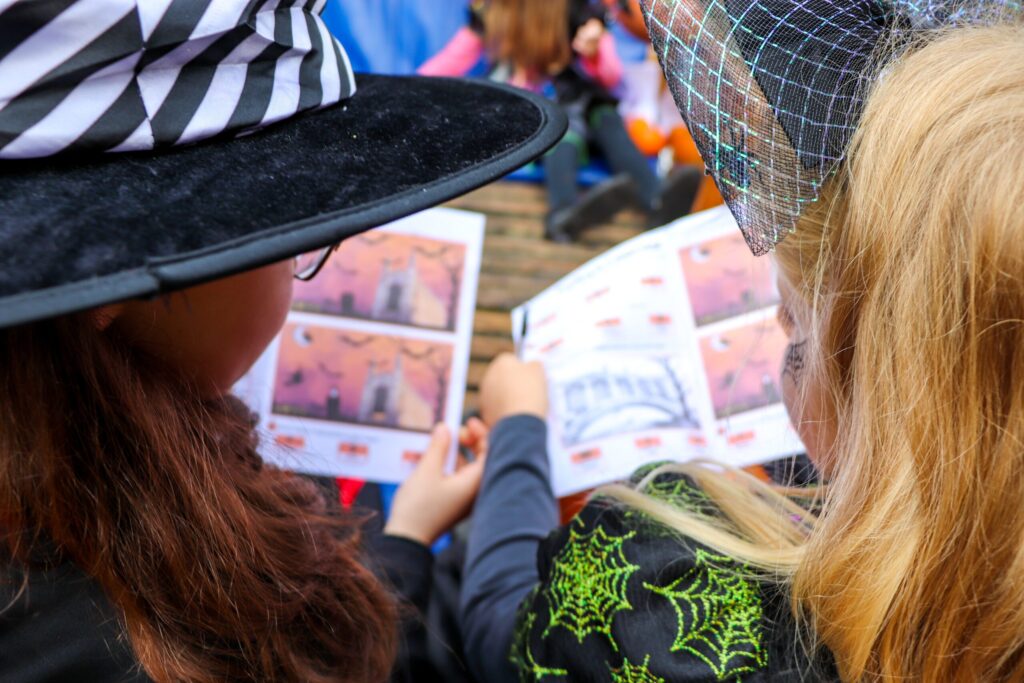 Children in witch costumes reading Halloween activity booklets during a punt tour in Cambridge.