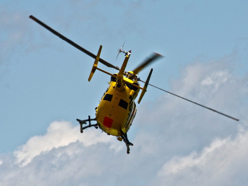 Yellow air ambulance helicopter flying against a blue sky with white clouds.
