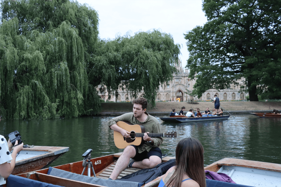 Liam Martin strumming an acoustic guitar from a punt for Music on the River on the Cam.