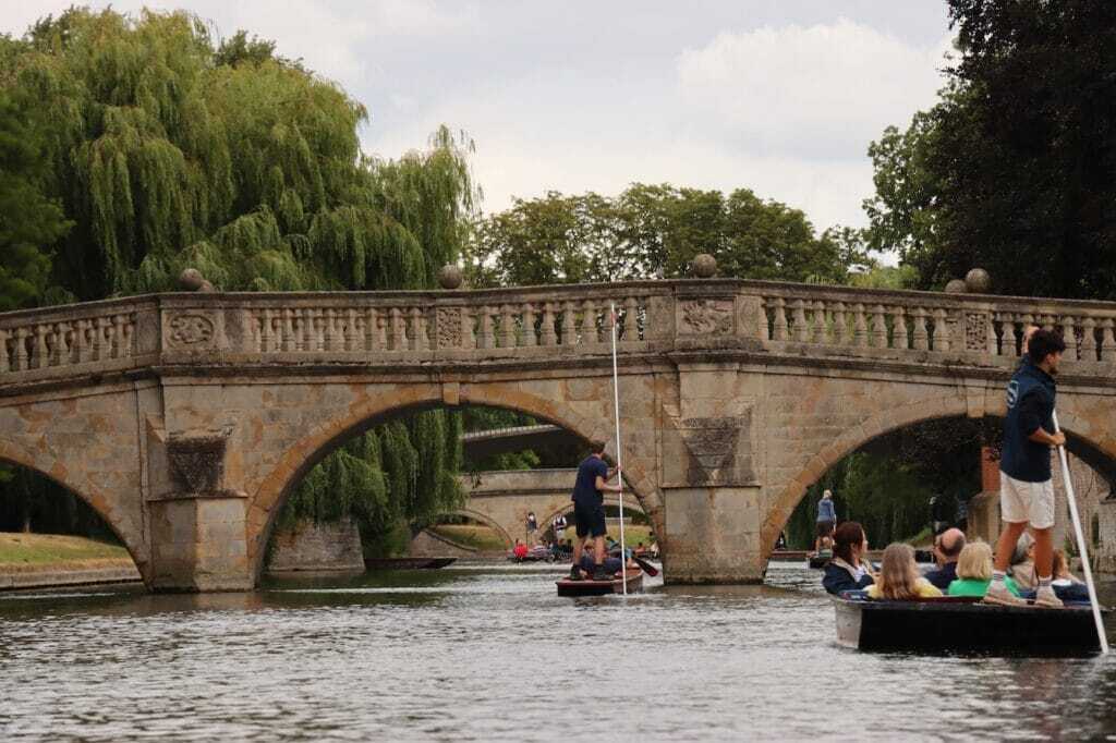 Punts gliding beneath the stone arches of Clare Bridge with willow trees behind, Cambridge